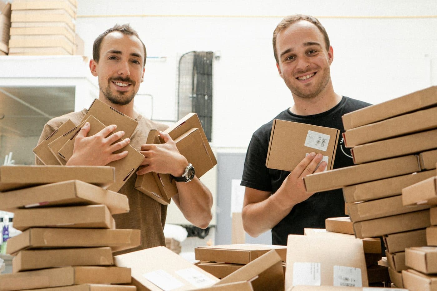 Dos personas sonriendo detrás de una pila de pedidos de su tienda online listos para despachar